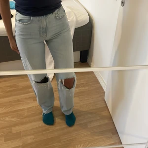 Ljusblå ripped jeans med raka ben - Säljer ett par ljusblå jeans med raka ben och stora slitningar vid knäna. Jeansen har klassisk femficksdesign, hög midja och är tillverkade i denim. Perfekta för en avslappnad och trendig look. Från ginatricot storlek 34!