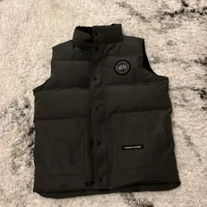 Svart dunväst från Canada Goose -   "Snygg väst i bra skick, perfekt för höstens alla äventyr! Inga defekter, redo att användas.  Jag vill sälja den eftersom använder inte den lika ofta och den börjar bli lite för liten. Har inte använt mycket bara lite i sommaren.