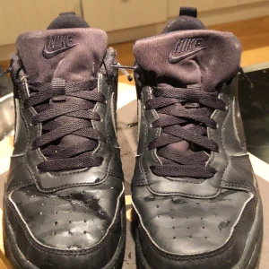Svarta Nike sneakers strl 38.5 - Säljer ett par helsvarta Nike sneakers med klassisk swoosh på sidan. Skorna har snörning, rund tå och är tillverkade i syntetmaterial och textil. Perfekta för dig som gillar en clean och stilren look. Om du har frågor kontakta mig gärna. OBS: priset går att sänka