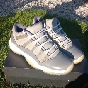 Air Jordan 11 Retro Low Grey - Säljer ett par Air Jordan 11 Retro Low i grått och vitt. Skorna har en snygg kombination av blankt och matt material, vita snören och en genomskinlig sula. Perfekta för dig som gillar klassiska sneakers med unik design. Använda men välvårdade.