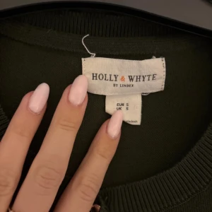 Mörkgrön kofta från Holly & Whyte - Snygg mörkgrön kofta från Holly & Whyte med rund halsringning och knappar framtill. Långärmad modell i mjuk bomull, perfekt att slänga över en topp eller klänning. Enkel och stilren design som funkar året runt.