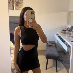 Svart tight cut out klänning - Säljer en svart tight kortklänning med cut out-detalj i midjan och ärmlös design. Klänningen har en rund halsringning och är tillverkad i ett stretchigt material som sitter snyggt på kroppen. Perfekt för dig som vill sticka ut med en trendig look.