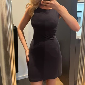 Kort klänning Gina tricot  - En stilren svart kortklänning med ärmlös design och rund halsringning. Klänningen har en figurnära passform och är tillverkad i ett mjukt, stretchigt material som sitter snyggt på kroppen!