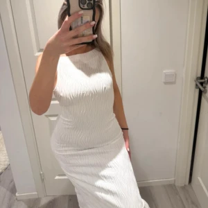 Vit långklänning med vågigt mönster - Säljer en vit långklänning med ett snyggt vågigt mönster. Klänningen är ärmlös och har en rak halsringning med smala axelband. Passformen är slim och tyget känns mjukt mot huden. Perfekt för dig som gillar stilrena och moderna looks.