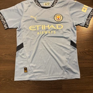 Manchester City matchtröja Puma S - Manchester Citys officiella matchtröja från Puma i ljusblått med klubbmärke och Etihad Airways-tryck på bröstet. Tillverkad i återvunnet material (Re-Fibre) och har korta ärmar samt svarta detaljer på sidorna och ärmslut.
