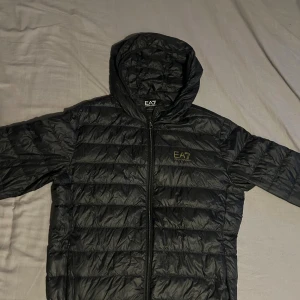 Svart pufferjacka från EA7 Emporio Armani - Svart tunn jacka från ea7 bra skick men ena fickan har tappat dragkedjan.