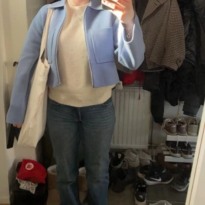 Ljusblå croppad overshirt från ARKET - Säljer en ljusblå croppad overshirt från ARKET med två stora bröstfickor och dragkedja framtill. Jackan är stickad i ett mjukt material och har klassisk krage samt långa ärmar. 