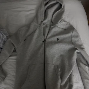 Grå hoodie från Ralph Lauren - Snygg grå hoodie från Ralph Lauren med dragkedja och klassisk logga på bröstet. Inga flaws alls och är i princip som ny. Till skillnad från många andra är denna äkta vilket du ser på detaljer som loggan men har tyvärr inget kvitto kvar. 