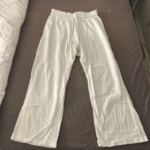 Vita vida linnebyxor med resårmidja - Säljer ett par vita linnebyxor med breda ben och resår i midjan. Byxorna har två fickor fram och två bak, vilket ger en chill och avslappnad vibe. Perfekta för varma dagar när du vill ha något luftigt och bekvämt.