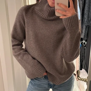 Brun polotröja från Wera - Mysig brun polotröja från Wera i 100% ull. Tröjan har en hög, ribbad polokrage och långa ärmar med breda muddar. Perfekt för kyliga dagar och enkel att styla med jeans eller kjol.