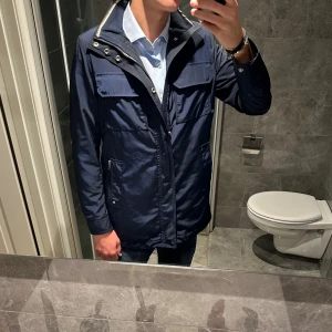 Marinblå lång regnjacka j.Lindeberg  - Schysst marinblå regnrock från j.Lindeberg. Jackan är i riktigt bra skick. Jag är 188cm på bilden. Hör av er vid funderingar;)