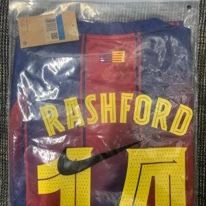 FC Barcelona Rashford Nike fotbollströja M - Säljer en officiell FC Barcelona fotbollströja från Nike med Rashford och nummer 14 på ryggen. Tröjan är blå och röd med gula detaljer, randigt mönster och tillverkad i Dri-FIT-material för bästa komfort. Perfekt för dig som älskar fotboll och vill sticka ut på planen.