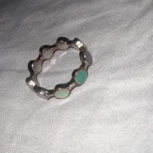 Vågig silverring med pastellfärgade detaljer - Unik vågig ring i silverfärgad metall med runda pastellfärgade inslag i grönt, ljusgrönt och ljuslila. Ringen har en cool, lekfull design som sticker ut och passar perfekt för dig som gillar färg och form. Perfekt accessoar för att lyfta din outfit.