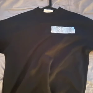 Moschino sweatshirt  - Svart sweatshirt från Moschino med silverfärgat logotryck på bröstet. Tröjan har rund halsringning och är tillverkad i 100% ekologisk bomull.  Storlek M. Väldigt bra skick. Fler bilder kan skickar om man vill. .