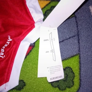 Arsenal Martinelli 11 Adidas tröja - Röd och vit Arsenal fotbollströja från Adidas med Martinelli och nummer 11 på ryggen. Tröjan har korta ärmar, Aeroready-material och officiella klubbmärken. Perfekt för dig som vill visa ditt stöd för Arsenal och Martinelli.