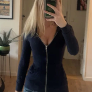 Mörkblå tight hoodie med dragkedja - Säljer en mörkblå hoodie med lång ärm och hel dragkedja framtill. Tröjan har en figurnära passform. Har varit en annan storlek innan men är omsydd i midjan så att den ska sitta tajtare,Är nu ungefärr en XXS-XS ungefär.