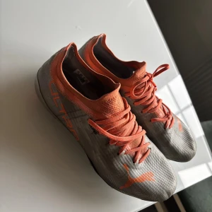 Puma Ultra fotbollsskor silver/orange - Säljer ett par grymma Puma Ultra fotbollsskor i storlek 38.5. Skorna är i silver med orange detaljer och snörning, samt har klassiska dobbar för bästa grepp på planen. Ovandelen är i lätt syntetmaterial som ger en tight och skön passform.