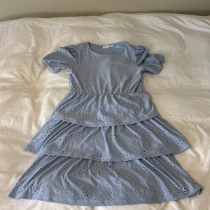 Ljusblå volangklänning med broderi - Superfin ljusblå klänning från Vila med broderade detaljer och volanger i tre lager. Klänningen har korta puffärmar och rund halsringning. Använd en gång. 