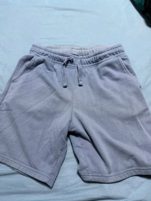 Grå mjukisshorts från 157, storlek M - Säljer ett par grå mjukisshorts från 157 i storlek M. De har elastisk midja med snörning, två sidofickor och en bakficka. Materialet är mjukt och skönt, perfekt för chill dagar eller träning. Klassisk loose passform och enkel design.