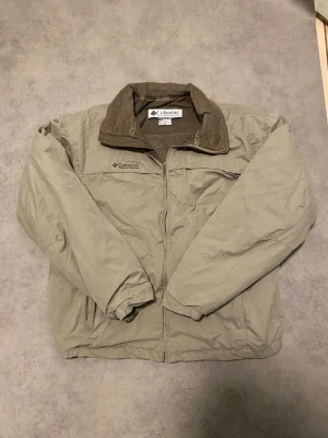 Vintage jacka från Columbia L - Säljer denna riktigt snygg vintage jackan från Columbia i storlek L. Jackan har en mjuk fleecefodrad krage, dragkedja framtill och två sidofickor. Perfekt för kyliga dagar och outdoor-aktiviteter. Diskret broderad logga på bröstet och klassisk look.