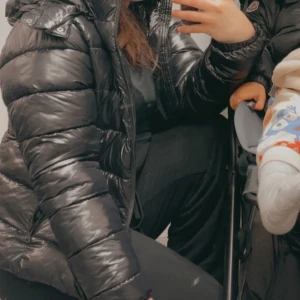 Lager157 Nikki dunjacka - Säljer en svart pufferjacka med glansig yta och långa ärmar. Jackan har dragkedja framtill och en klassisk pufferlook som är både varm och trendig. Perfekt för kalla dagar och enkel att styla till olika outfits. Storlek är som en S.