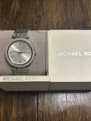 Michel Kors Klocka - Säljer Michel Kors Darci Silver Klocka. Helt oanvänd i orginal kartong. Köpt på smycka för 3249kr, säljer för 2000kr.