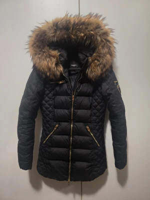 Rockandblue Vinterjacka - Säljer en stilren och varm vinterjacka från Rockandblue. Jackan är svart och har en lyxig huva. Väldigt skön och passar perfekt för kalla vinterdagar. Jackan är köpt för 3500 kr och är äkta. Jackan är välvårdad och sparsamt använd. Dragkedjor och detaljer är i guld som ger en exklusiv känsla. En tidlös modell som håller i  många år.  Storlek: 34  Färg: Svart  Märke: ROCKANDBLUE  Skick: Mycket fint skick  Pris: 1750  Hör av dig vid intresse eller funderingar!