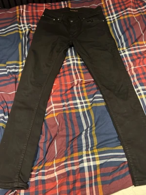 Svarta denim Nudie Jeans - Svarta jeans från Nudie Jeans i storlek 32/32. Modellen har en bra passform med klassisk femficksdesign och dragkedja. Materialet är jeans och färgen är helsvart, vilket ger en clean och stilren look.