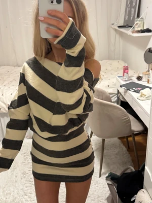 Randig offshoulder stickad klänning - Superfin kort långärmad stickad klänning med breda svarta och beige ränder. Modellen är offshoulder med lång ärm och en tight passform som framhäver figuren. Perfekt för dig som gillar en avslappnad men ändå trendig stil. beige, svart. Går att ha på olika sätt som syns på bilderna!!🧡🧡