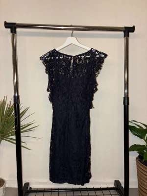 Spetsklänning  - Svart klänning med vacker spets. Klänningen har en elegant, figurnära form och sitter lite nästan knälång. Materialet är spets med fina mönster och den har en rund halsringning. Elegant but daring look.