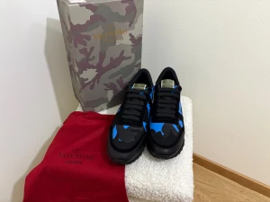 Valentino Garavani Rockrunner sneakers - Säljer ett par Valentino Garavani Rockrunner sneakers i svart och blått med coolt kamouflagemönster. Skorna har snörning, rund tå och platt sula. Materialmix med inslag av skinn och syntet. Kommer med originalkartong och röd dustbag.