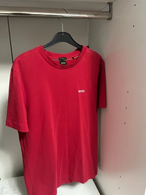 Röd BOSS t-shirt i bomull - Snygg röd t-shirt från BOSS med klassisk rund hals och korta ärmar. T-shirten har en stilren logotyp på bröstet och är gjord i mjuk bomull med stretch för extra komfort. Perfekt för dig som gillar enkel och clean stil.