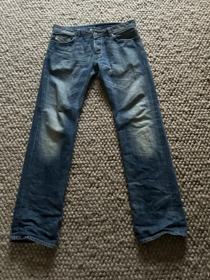 Blå jeans från Diesel Industry - Säljer ett par klassiska blå jeans från Diesel Industry med snygga slitningar på framsidan och detaljerade bakfickor. Jeansen har rak passform och normal midja, tillverkade i slitstarkt bomullsmaterial. Perfekt för dig som gillar en tidlös och cool denimlook.