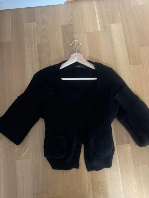 Svart stickad kofta från SHEIN - Säljer en svart, ribbstickad kofta från SHEIN i storlek XS. Koftan har långärmade, lite vidare ärmar och två praktiska fickor framtill. Perfekt att slänga över en t-shirt eller linne för en chill look.