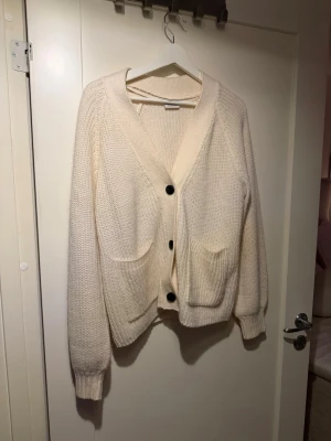 Beige stickad kofta från Noisy May - Mysig beige stickad kofta från Noisy May med stora svarta knappar och två framfickor. 