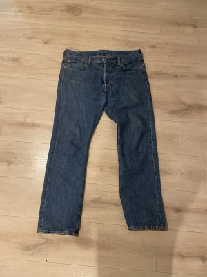 Levi's 501 jeans blå - Klassiska Levi's 501 jeans i mörkblå denim med raka ben och fem fickor. Snyggt läderpatch bak i midjan och ikonisk röd Levi's-tagg på bakfickan. Perfekt passform och tidlös stil, tillverkade i slitstarkt bomullsmaterial.