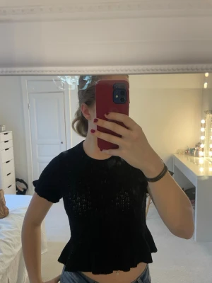 Svart stickad topp - Supersöt svart stickad topp från H&M Divided i storlek S. Toppen har korta ärmar, rund halsringning och volangkant nertill och i slutet av ärmarna. Den är lätt genombruten i stickningen (se sista bild)