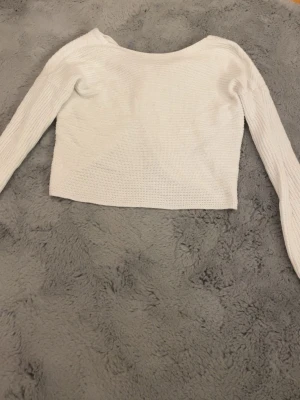 Vit croppad stickad tröja med knut - Superfin vit croppad stickad tröja med lång ärm och snygg knutdetalj och öppen rygg. Perfekt till jeans eller kjol för en chill men ändå trendig look. Tröjan har en lätt ribbad struktur och är riktigt skön att ha på sig. Kan eventuellt tänka mig gå ner i pris