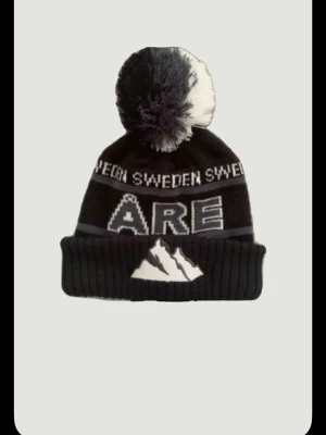 Åre mössa - Bilden visar en svart och vit mössa med texten 'ÅRE' och 'SWEDEN' samt en bergsillustration, men ingen väst finns med. Skriv vid minsta fundering. Pris ej hugget Sten 🪨