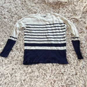 Randig långärmad tröja från H&M - Säljer en tunn långärmad tröja från H&M i storlek S. Tröjan är vit med marinblå horisontella ränder och bredare marinblå partier längst ner och vid ärmsluten.  Materialet är 50% akryl och 50% viskos, vilket gör den mjuk och lätt.