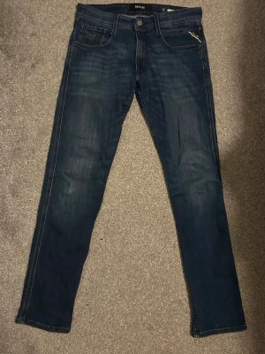 Replay mörkblå jeansbyxor slim - Snygga mörkblå jeansbyxor från Replay med klassisk femficksdesign och diskreta slitningar. Modellen har slim passform och raka ben, perfekt för dig som gillar en stilren look. Materialet är mjukt jeans och byxorna har dragkedja och knapp i midjan.