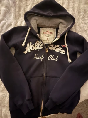 Hollister zip up hoodie - Mörkblå zip up hoodie med dekorativ text. Inga defekter alls, som ny