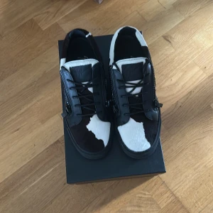 Giuseppe Zanotti sneakers med pälsdetaljer - Unika sneakers från Giuseppe Zanotti i svart och vitt med coolt koskinnsmönster. Skorna har snörning, dragkedjor på sidorna och detaljer i skinn. Pälsdetaljerna ger en lyxig känsla och den svarta sulan gör dem extra stilrena. Dem är helt nya jag har använt dom 2 gånger. Om nån är sugen så hör ev er till Millie Diop på plock eller skicka ett dm till mig.
