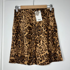 Leopardmönstrad kjol från Bik Bok - Supersnygg kort kjol från Bik Bok med leopardmönster i bruna och svarta toner. Kjolen har en lätt utsvängd form och är gjord i ett glansigt, mjukt polyestertyg som känns lyxigt. 