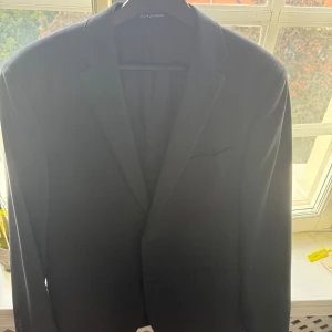 Mörkblå kavaj Oscar Jacobson EU 50 - Snygg mörkblå kavaj från Oscar Jacobson, modell Floyd Suit med comfort stretch. Klassisk design med smal krage och innerfoder med logotyp. Perfekt passform och stilren look, passar dig som vill ha en clean och modern vibe. Endast kavajen.