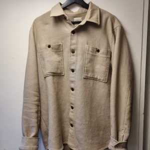 Beige overshirt/skjortjacka - Snygg beige overshirt i bomull. Nyligen köpt så aldrig använd pga att den var lite för stor. Perfekt nu till hösten, vår eller sena sommarkvällar. Hör av er för mer frågor