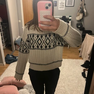 Vit stickad tröja med svart mönster - Supermysig vit stickad tröja med svart geometriskt mönster över bröstet och ärmarna. Tröjan har rund hals, ribbade muddar och en lite loose passform.