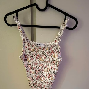 Blommig smockad linnetopp  - Supersöt smockad linnetopp från FB sister med blommigt mönster i rosa, gul och grön på vit botten. Toppen har smala, rynkade axelband och figurnära passform. Perfekt för varma dagar.