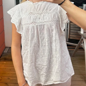 Vit blus  - Superfin vit blus i tunn bomull med broderade prickar, spetsdetaljer och volangärmar. Blusen har en lös passform och rund halsringning med liten volangkant. Passar mig som brukar ha xs-s!!