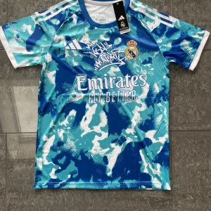 Real Madrid x Adidas blå fotbollströja  - Säljer en Real Madrid fotbollströja från Adidas i blått och vitt camouflagemönster. Tröjan har korta ärmar, rund hals och broderat klubbmärke. Materialet är lätt och andas, perfekt för träning eller match. Snyggt tryck med Emirates Fly Better på bröstet.